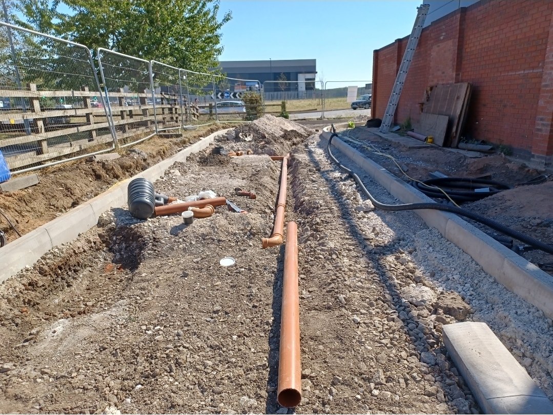 Groundworks beside a building with pipework and changing ground levels